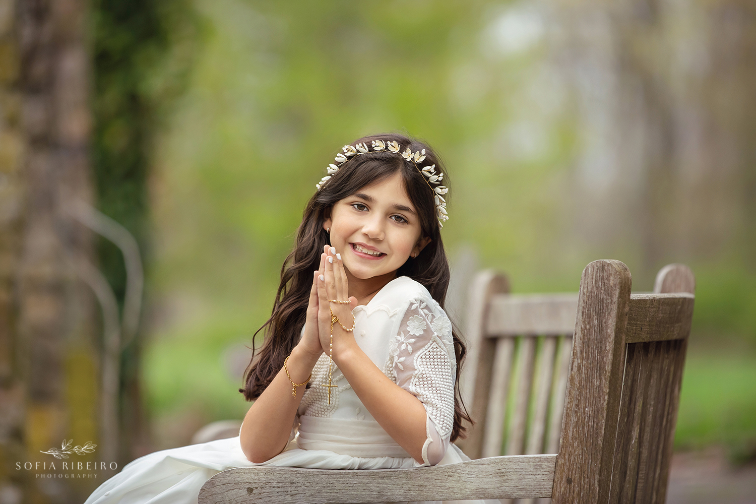 A LITTLE GIRL POSES IN HER COMMUNION DRESS WITH PRAYER HANDS