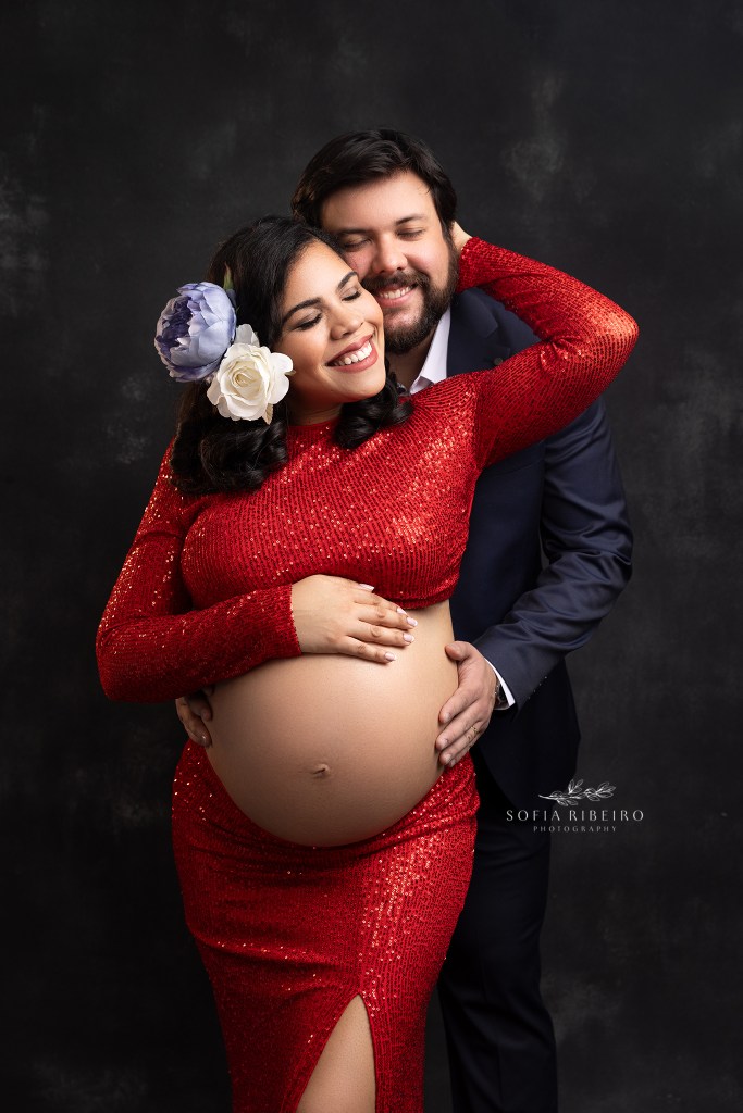 mom celebrates her dominican heritage in a red dress complete with blue and white flowers in her hair, showing off her baby bump