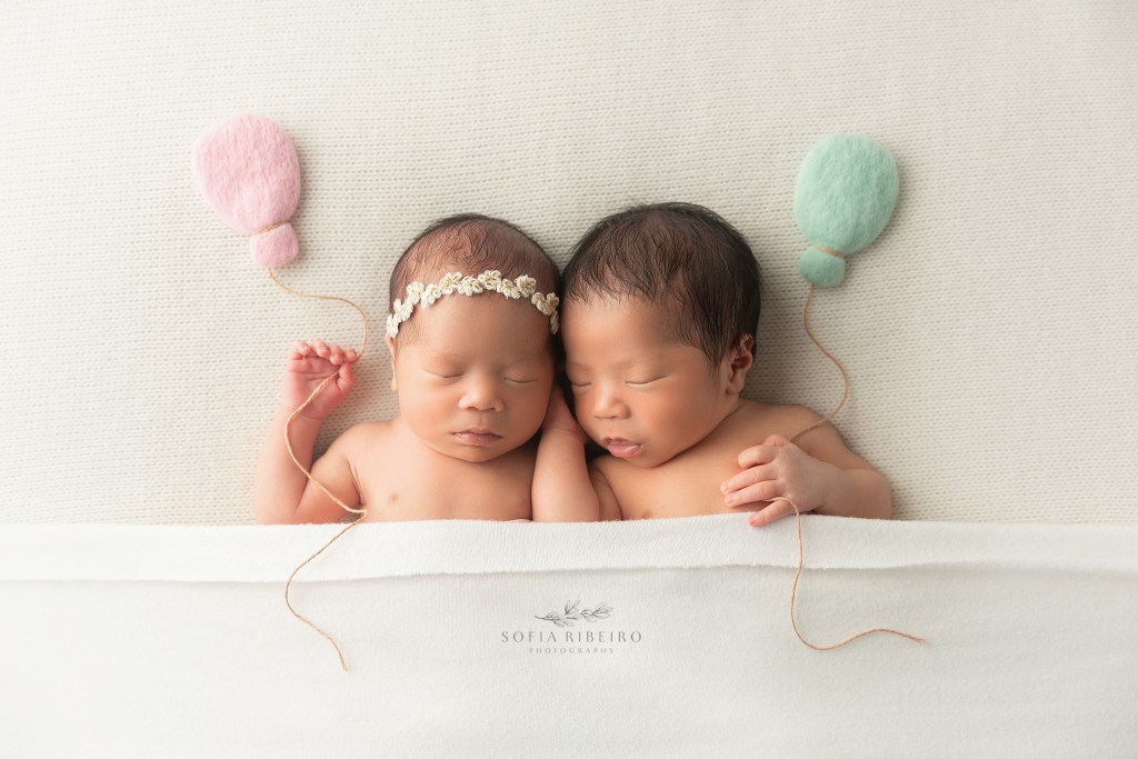 newborn twin siblings hold felted balloon props during their newborn photos in nj
