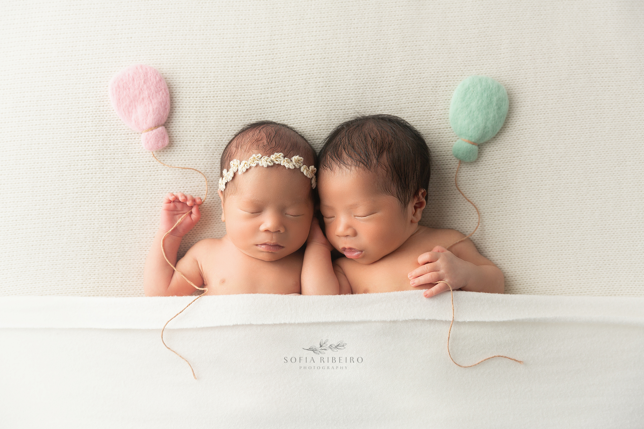 newborn twin siblings hold felted balloon props during their newborn photos in nj
