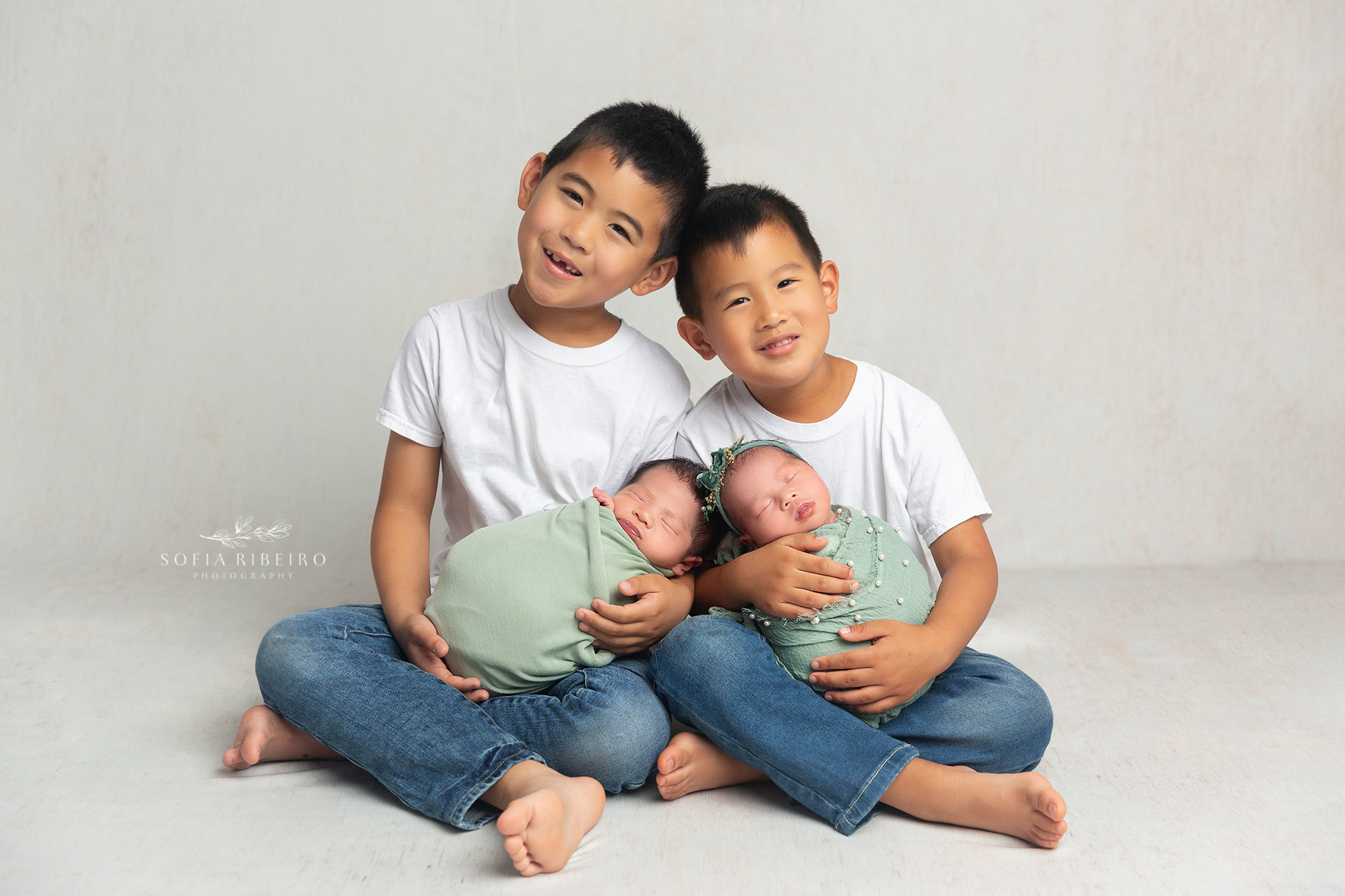 older brothers each hold one of their twin newborn siblings during a newborn photo session in nj
