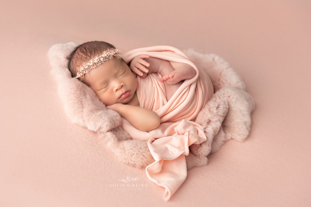 newborn twin girl is posed in a pink wrap and fur during her newborn photo session