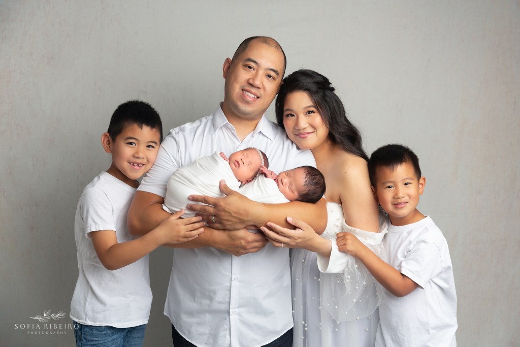mom and dad hold their newborn twin babies while big brothers snuggle on either side of them during a photo session in nj