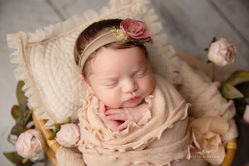 a newborn baby girl is posed sleeping sweetly in a basket prop with cream and peach colors for newborn photos in nj