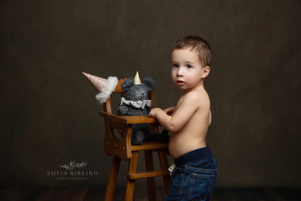 LITTLE BOY WITH TEDDY BEAR IN A HIGH CHAIRAND BIRTHDAY HAT CELEBRATES HER SECOND BIRTHDAY AFTER TAKING PHOTOS WITH NJ CHILDRENS PHOTOGRAPHER IN STUDIO