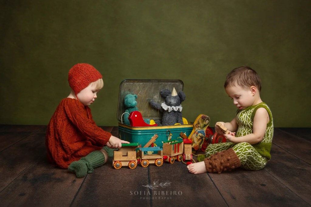 SIBLINGS PLAY WITH A CASE OF VINTAGE TOYS IN HANDKNIT OUTFITS AFTER A SESSION WITH A NEW JERSEY CHILDRENS PHTOOGRAPHER