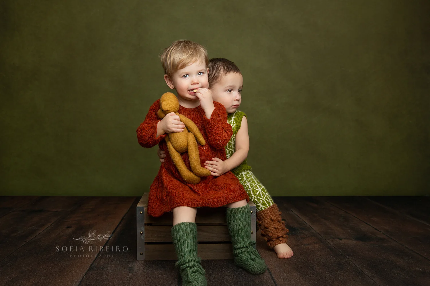 SIBLINGS HUG EACH OTHER IN HANDKNIT OUTFITS SITTING ON A BOX AFTER A SESSION WITH A NEW JERSEY CHILDRENS PHTOOGRAPHER