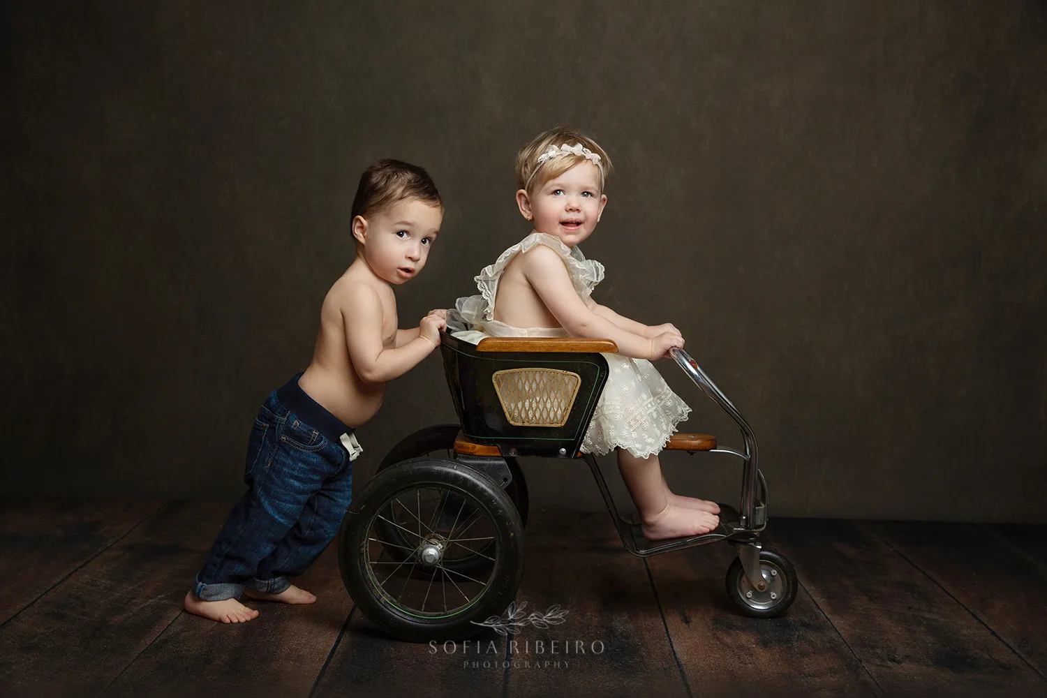 LITTLE BROTHER PUSHES SISTER IN A VINTAGE BLACK STROLLER WHILE TAKING PHOTOS WITH A NJ CHILDRENS PHOTOGRAPHER