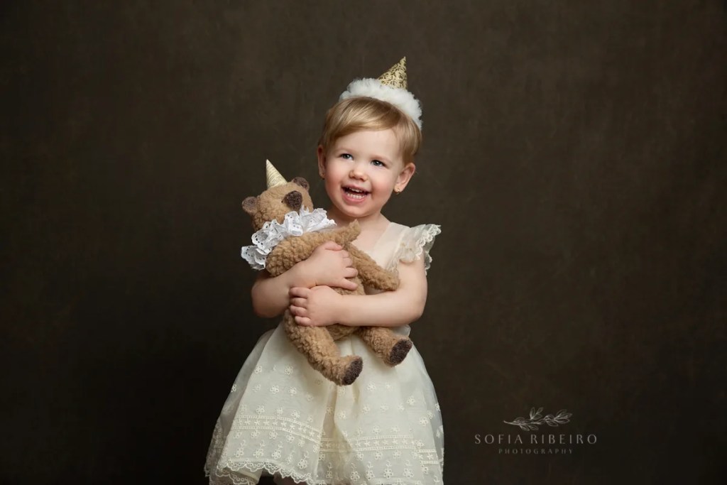 LITTLE GIRL WITH TEDDY AND BIRTHDAY HAT CELEBRATES HER SECOND BIRTHDAY AFTER TAKING PHOTOS WITH NJ CHILDRENS PHOTOGRAPHER IN STUDIO