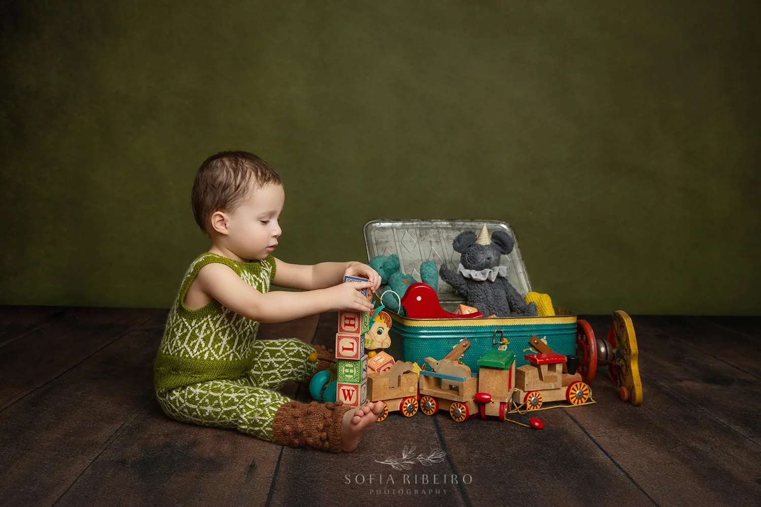 LITTLE BOY IN HANDKNIT OUTFIT PLAYS WITH VINTAGE TOYS AFTER TAKING PHOTOS WITH NJ CHILDRENS PHOTOGRAPHER IN STUDIO