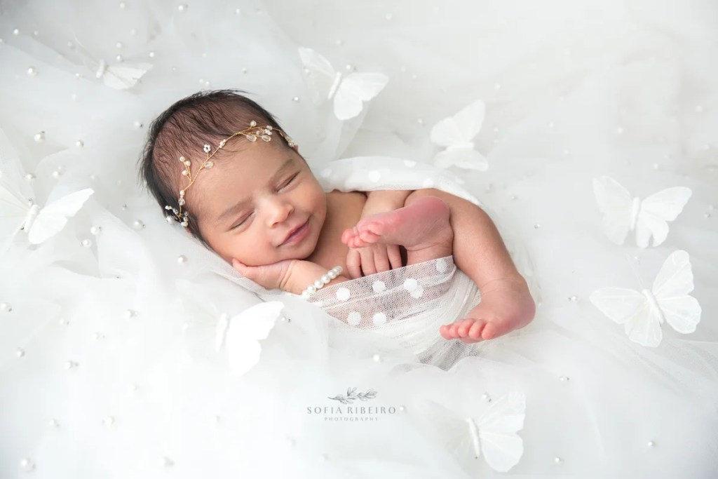 a newborn baby girl is posed on a white backdrop with tulle and butterflies surrounding her