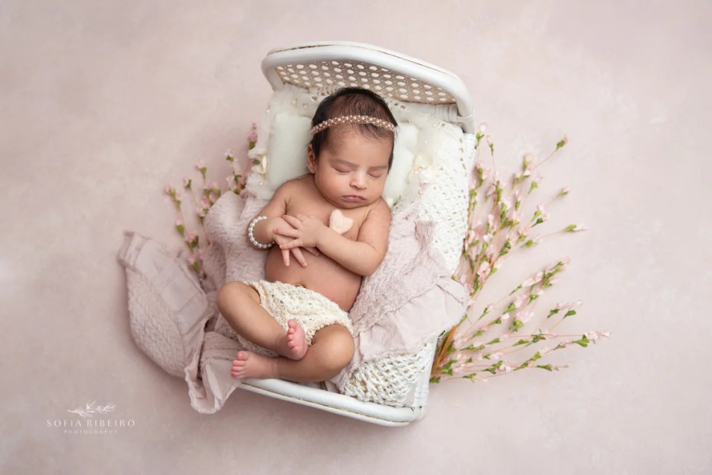 newborn baby girl is posed in a bed prop holding a heart prop in nj