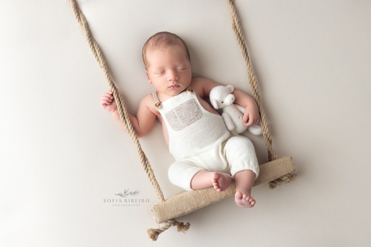 baby is posed on a fake swing prop with a bear during his photo session in new jersey