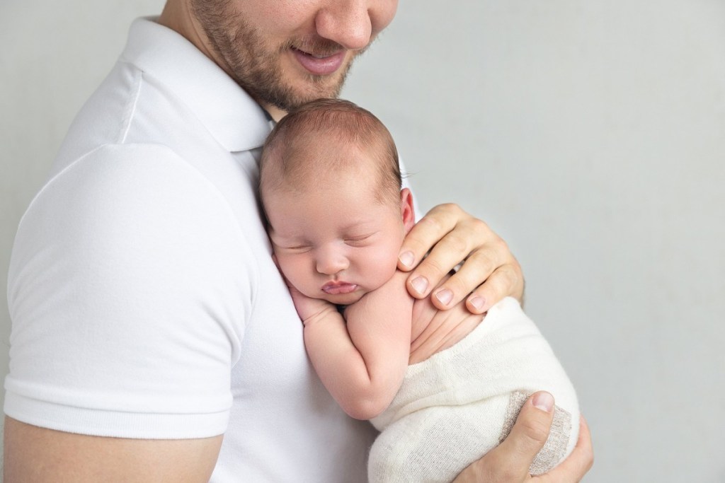 A newborn baby sleeps on dad's chest in a studio after attending baby classes nj