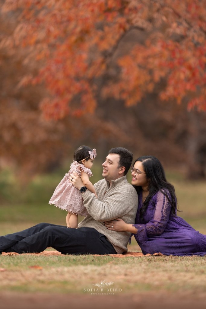 mom dad and baby smile together before taking photos during a fall family session in nj