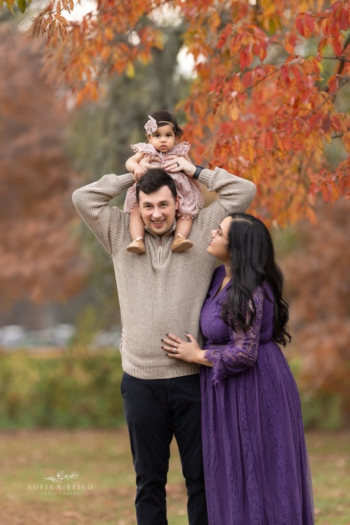 mom dad and baby smile together before taking photos during a fall family session in nj