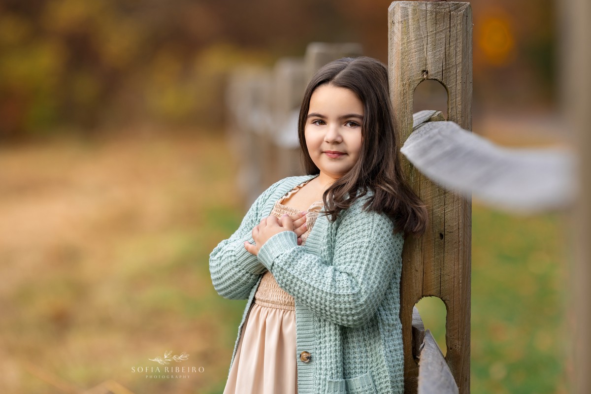 little girl poses against a fence during a childrens photo session in nj