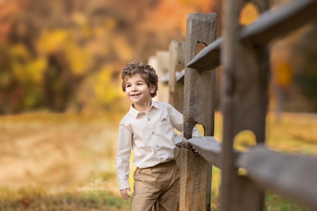 little boy poses against a fence during a childrens photo session in nj