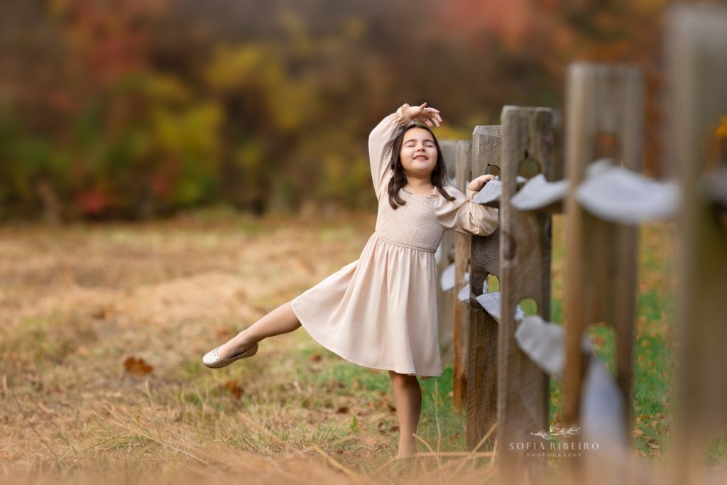 little girl poses in a ballet pose against a fence during a childrens photo session in nj
