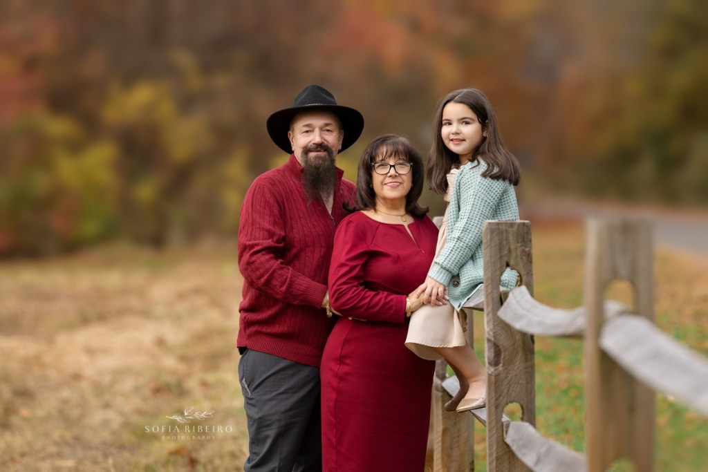 grandparents pose with granddaughter on fence during a family session