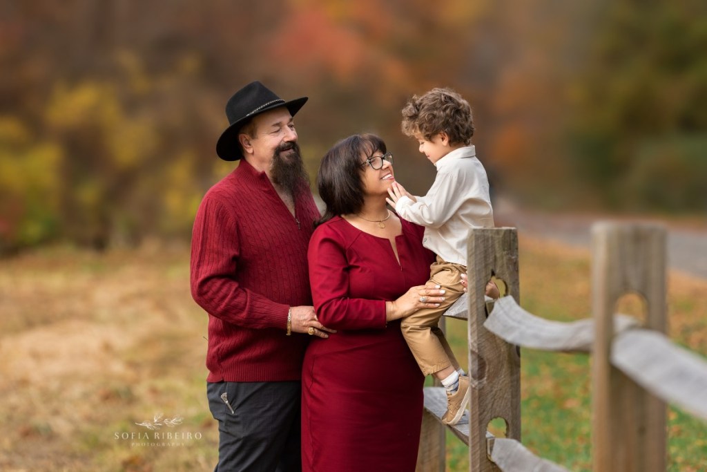 grandparents pose with grandson on fence during a family session