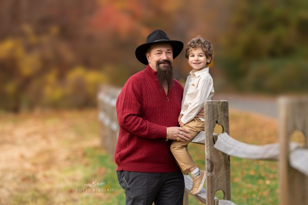 grandfather poses with grandson on fence during a family session