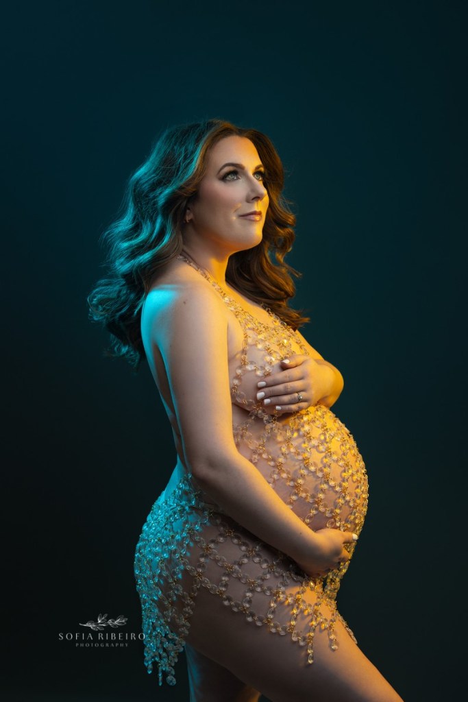 pregnant mom poses in a crystal dress against a dark background during a maternity session in nj