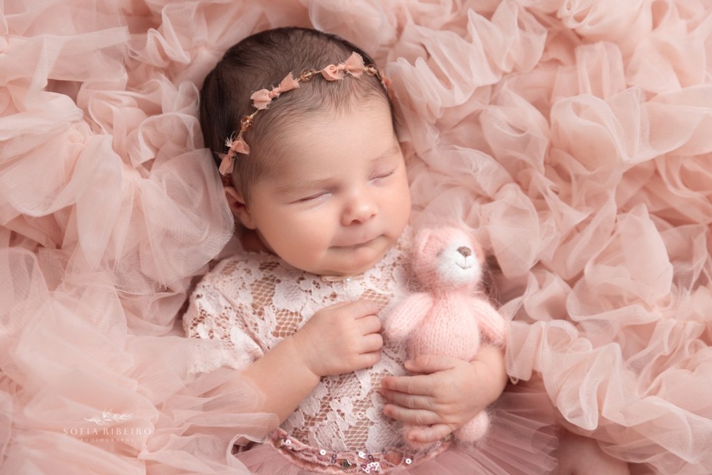 baby girl smiles in her sleep with a pink teddy bear before her newborn photo session