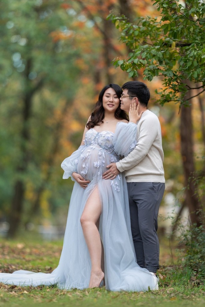 A mom to be holds her bump with her husband as he leans in for a kiss