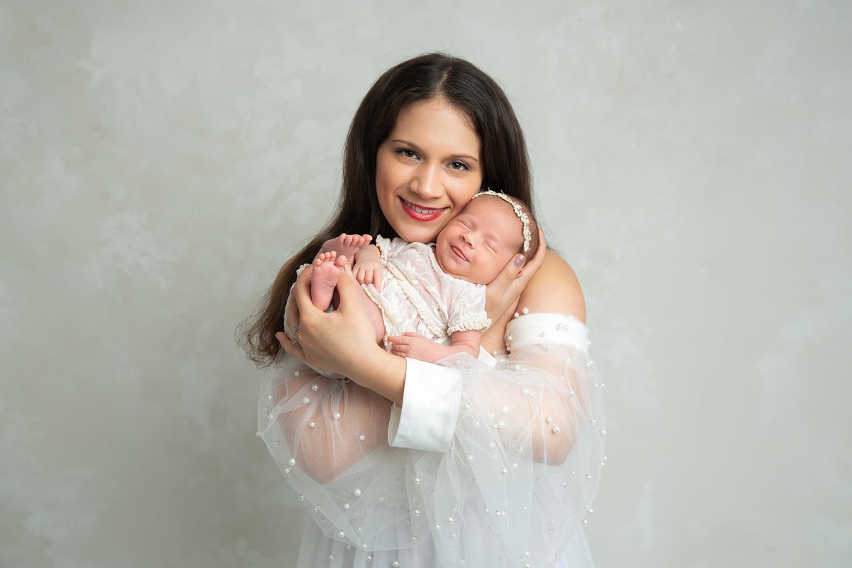 A happy mom cradles her smiling newborn baby against her cheek in a studio