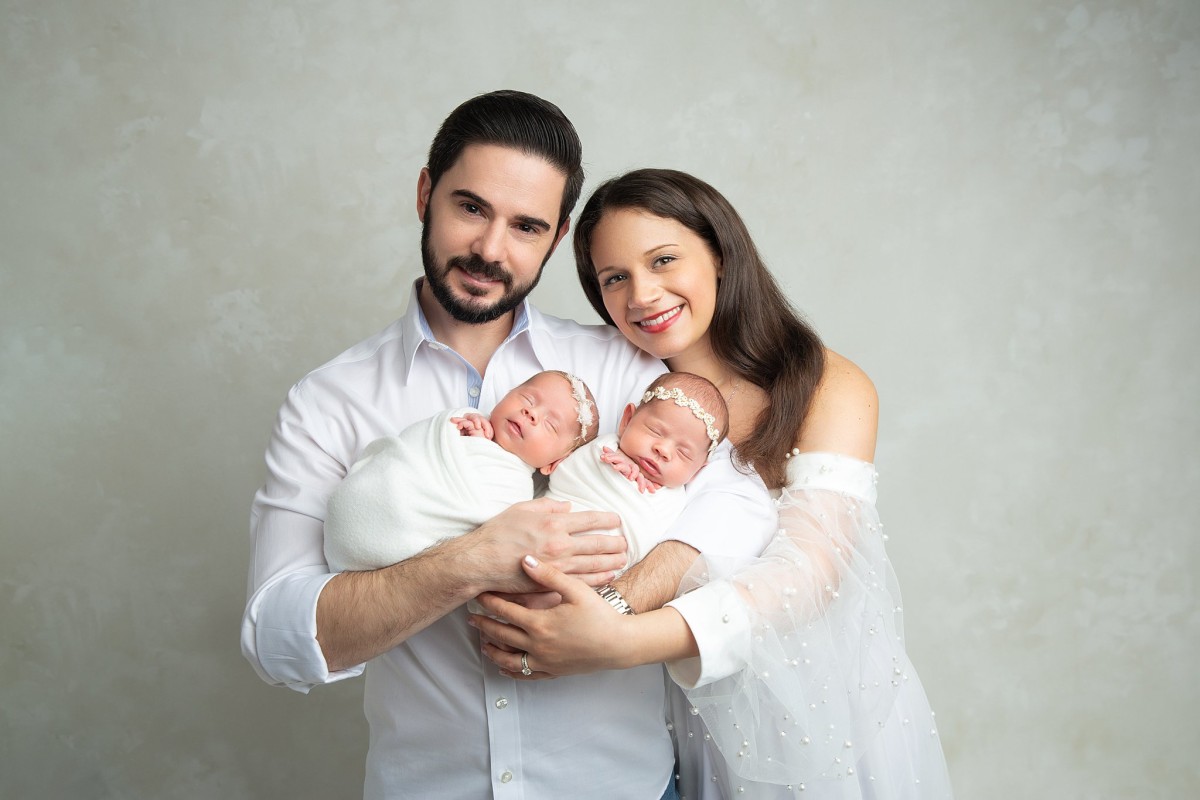 Happy parents stand in a studio holding their sleeping newborn baby twins before attending baby swim classes nj