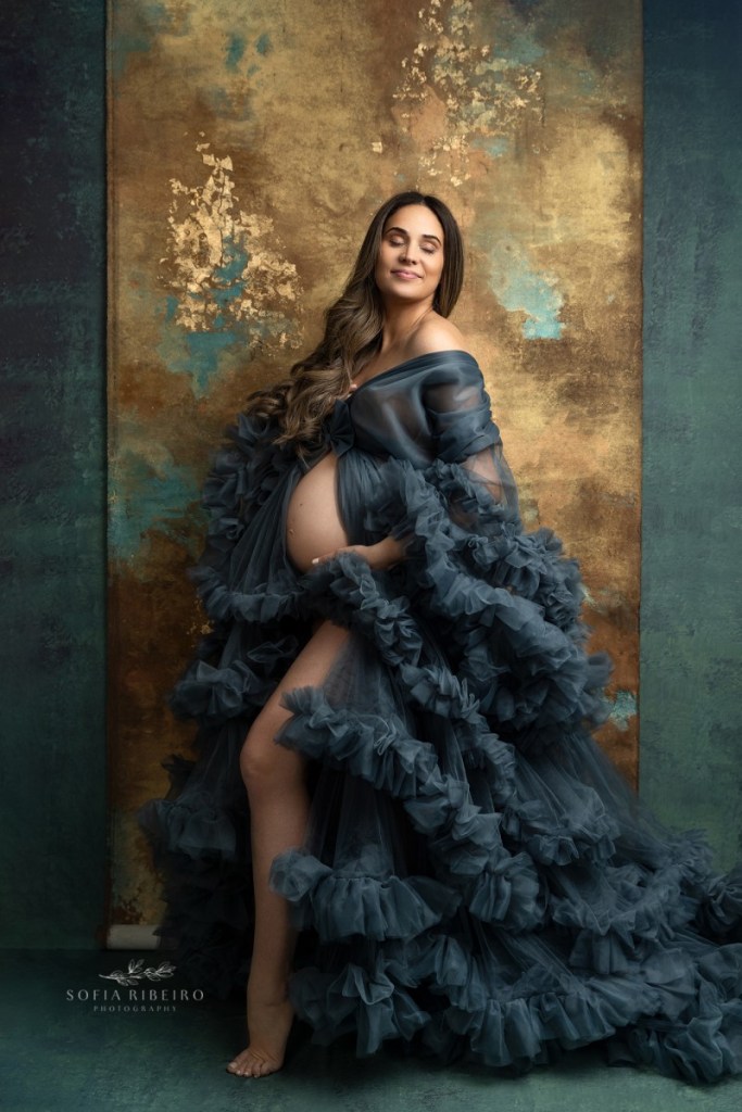 mom poses in a teal robe against a gold background during a nj maternity session