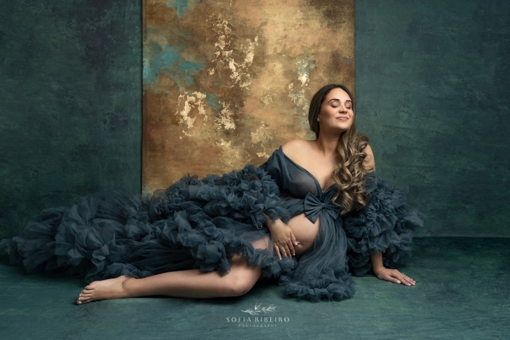 mom poses in a teal robe against a gold background during a nj maternity session