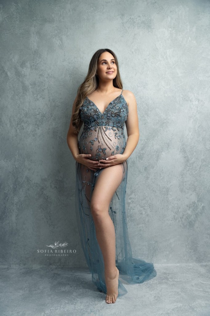 mom holds her belly in a blue beaded dress during a studio maternity session in nj