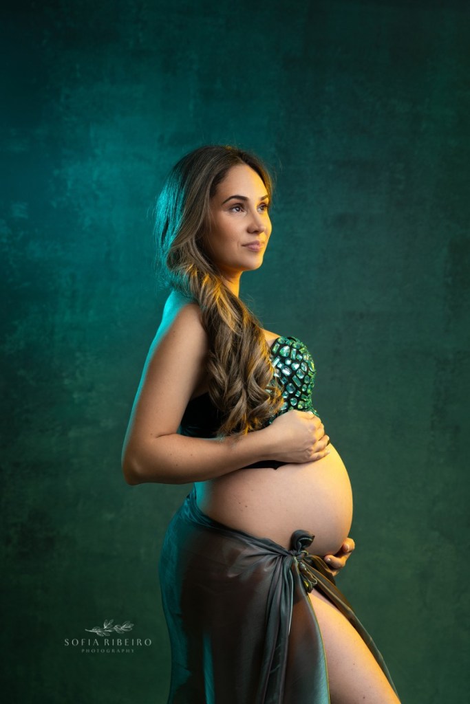 mom swishes her hair while wearing a bejewled green corset during a maternity session with a nj maternity photographer