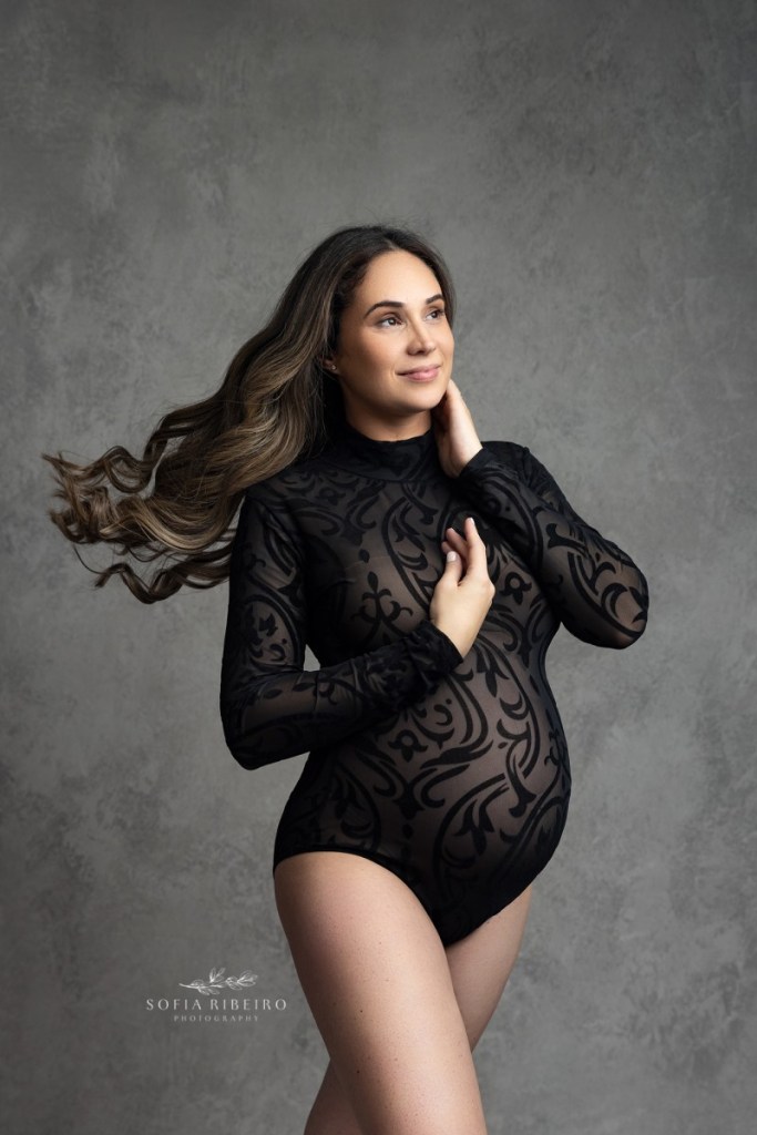 mom's hair blows in the wind in a black bodysuit for maternity photos