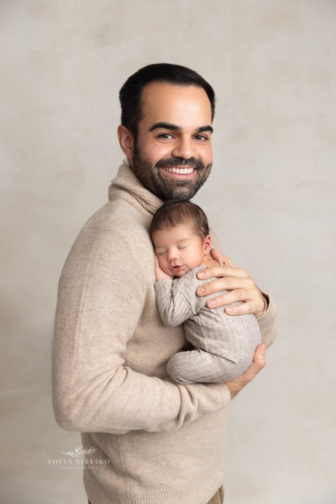dad smiles with joy at his newest baby boy, holding him against his chest