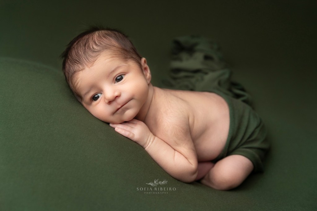 baby lies on a green posing fabric awake during his newborn session