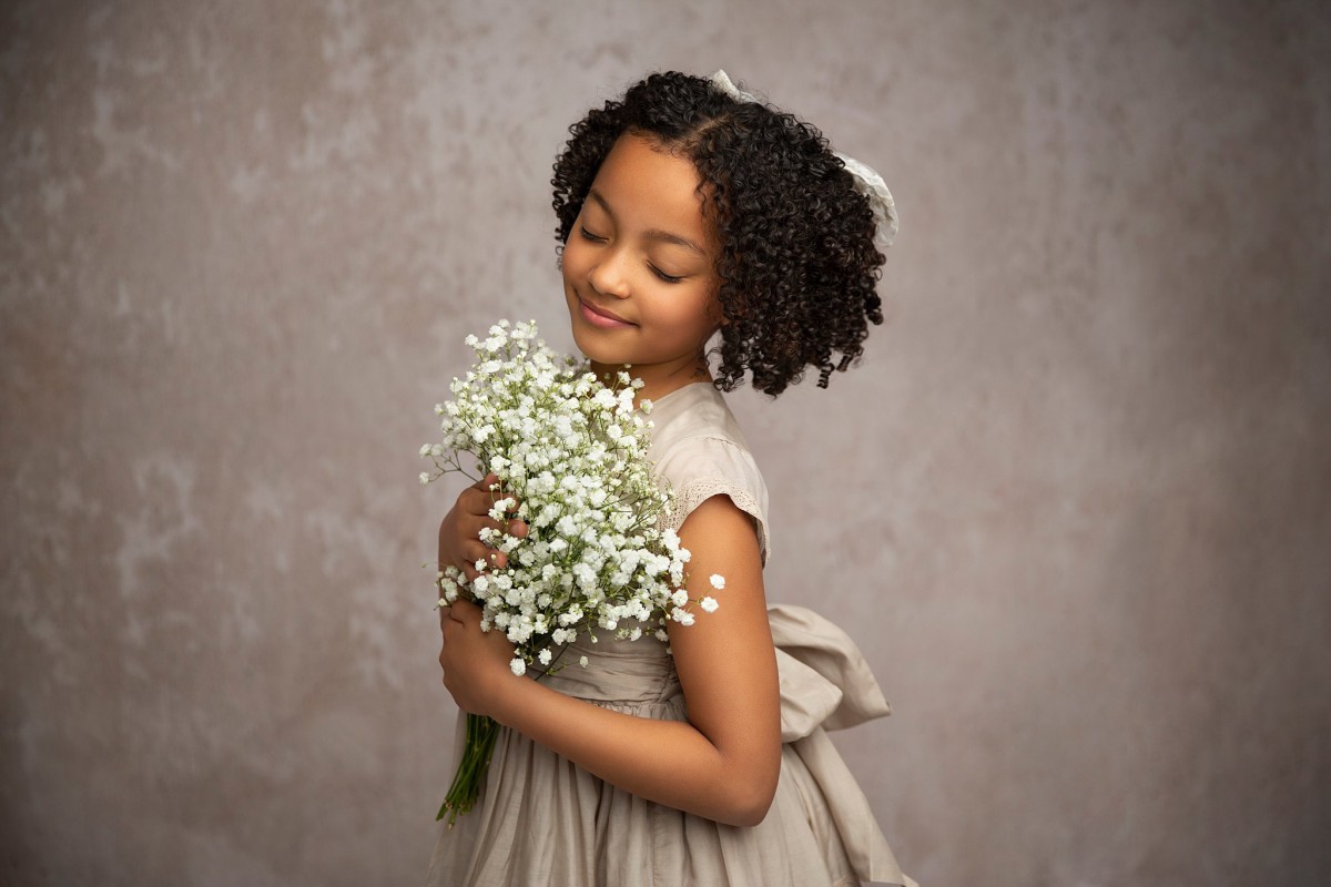 A young girl stands in a studio smelling a bundle of flowers in a dress after visiting francis henri