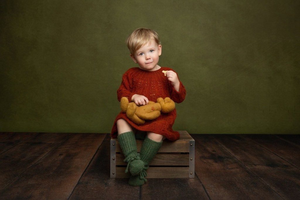 A young girl in a knit red dress sits on an apple box in a studio before visiting an indoor playground north jersey