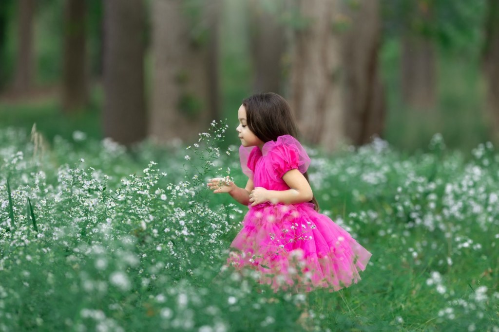 child smells some flowers in a field wearing a pink dress in nj during a portrait session with an nj photographer