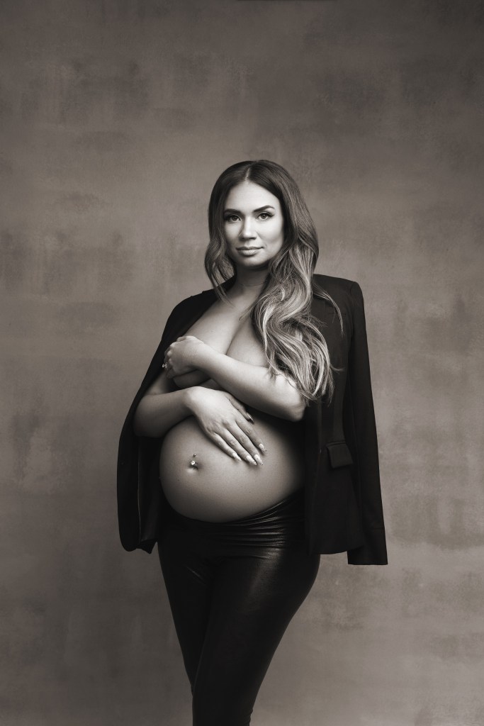 mom poses with attitude in an open black blazer on an apple box, with heels and leather tights during a maternity session in nj black and white version of photograph