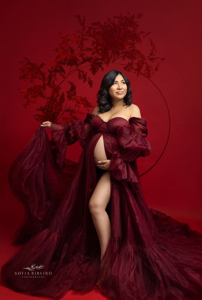 mom holds her red dress open, highlighting her bump in between poses for a maternity session