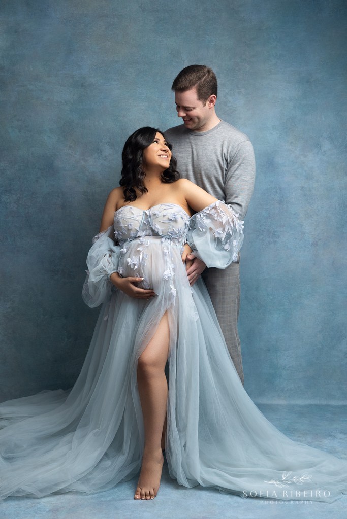 mom and dad cuddle together in a sweet moment during their maternity session dressed in shades of blue