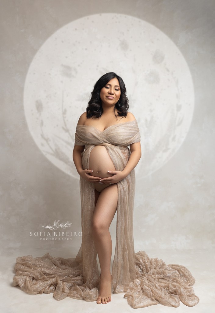 mom looks like a golden goddess with a halo and gold fabric dress while waiting on a photo during her maternity session
