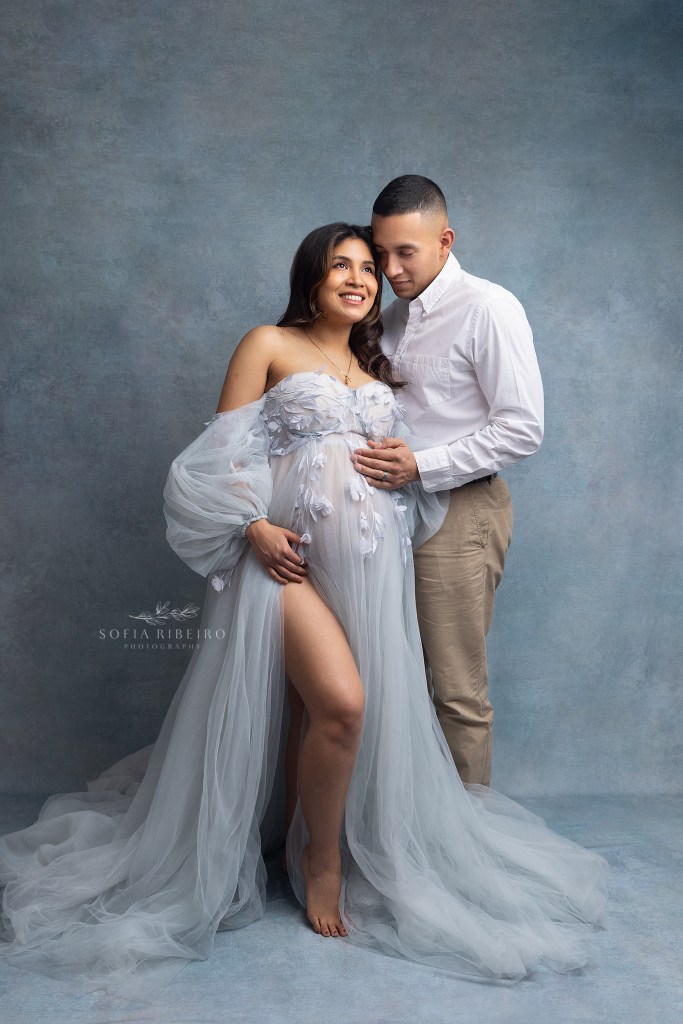 mom and dad pose lovingly together in formal attire while dad holds moms belly for a maternity portrait