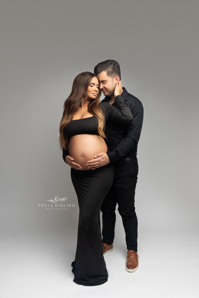 mom holds dads face towards her, both wearing black outfits during a maternity session in nj