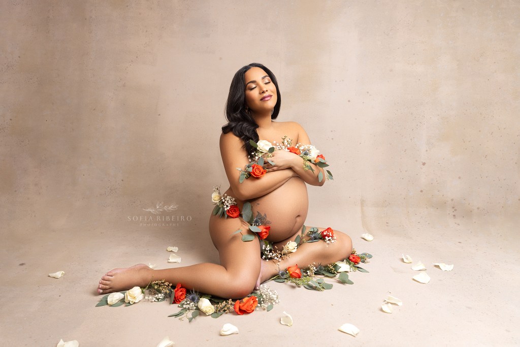 beautiful mom poses with orange cream and green flowers with a serene look in between portraits during a jersey city nj maternity session