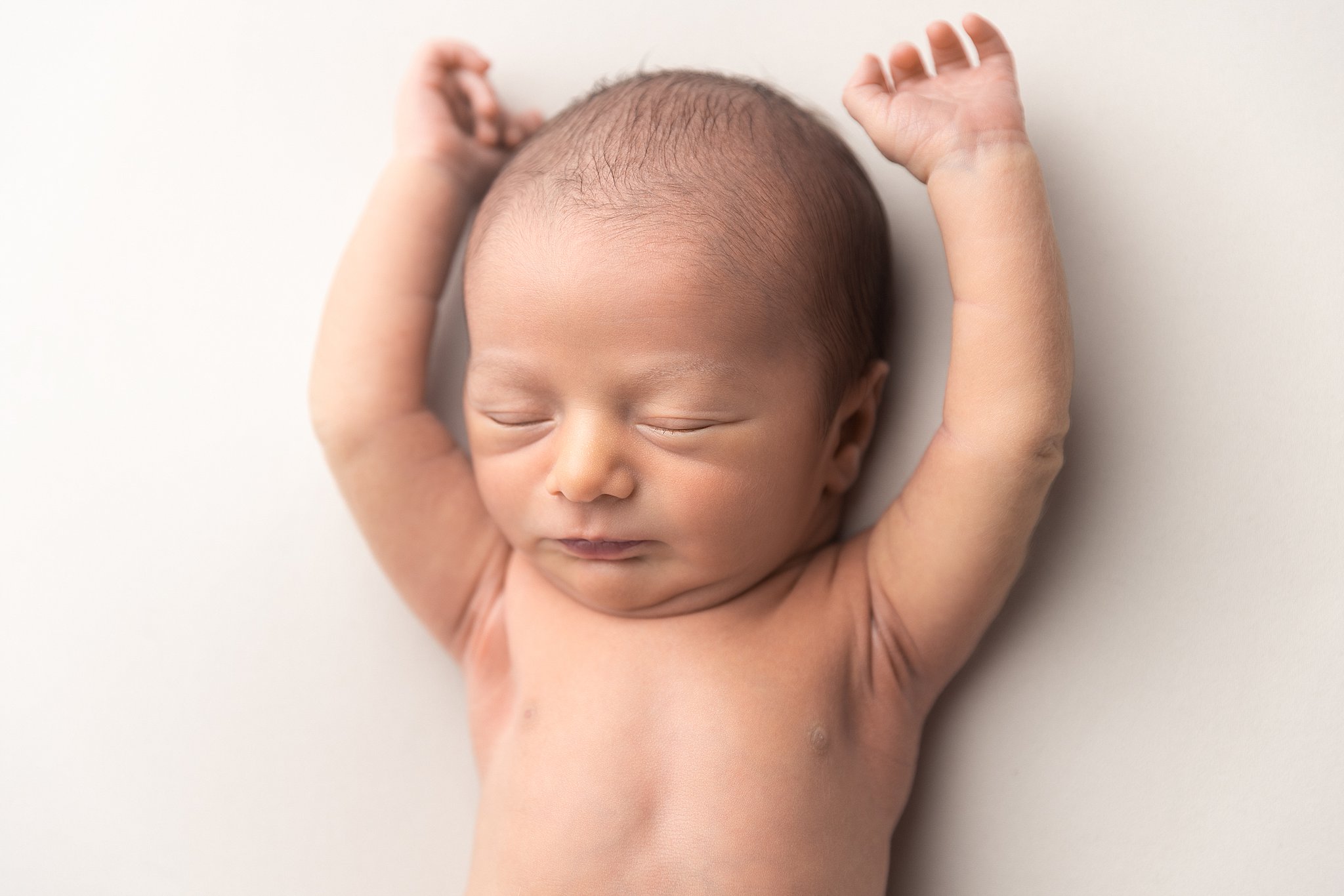 A newborn baby sleeps with hands up on a white bed