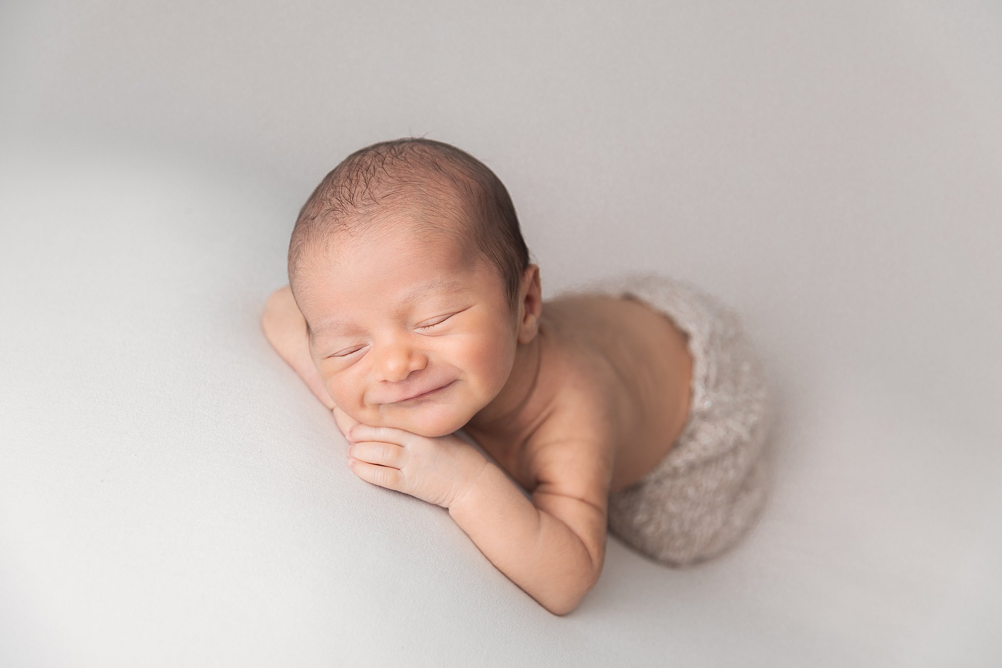 A newborn baby smiles in its sleep while laying on its hands thanks to lactation consultants NJ